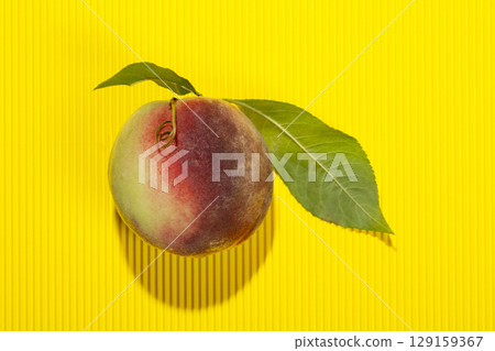 Ripe peach with leaves on a yellow background Ripe peach with leaves on a yellow background 129159367