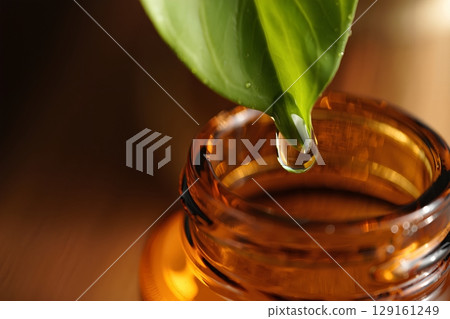 Single droplet falling from leaf into amber glass bottle, natural skincare product making process visualization Single droplet falling from leaf into amber glass bottle, natural skincare product making process visualization 129161249
