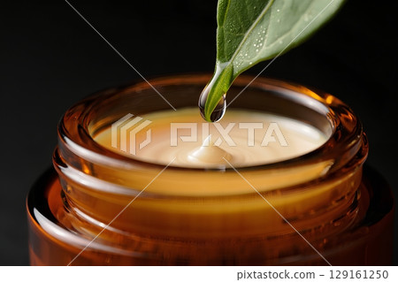 Close-up of water drop from green leaf into cosmetic bottle, organic beauty product concept 129161250