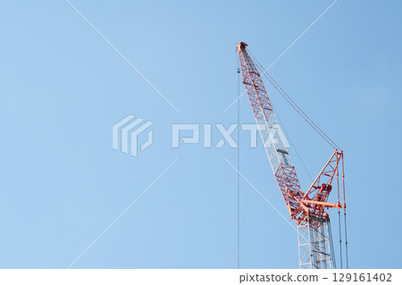 The arm of a large crane stretched out towards the blue sky 129161402