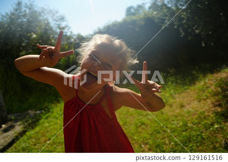 Playful Girl Making Peace Signs in Sunny Garden 129161516