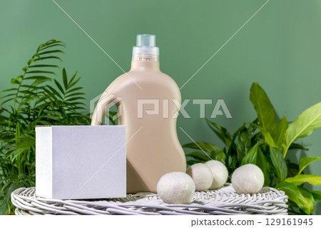 Natural laundry detergent mockup. Bottle of washing gel or fabric softener and box with detergent powder on white laundry basket on a green background with green leaves. Front view Natural laundry detergent mockup. Bottle of washing gel or fabric softener and box with detergent powder on white laundry basket on a green background with green leaves. Front view 129161945