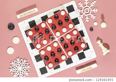 Winter holidays with board games. Various board games on a pink background with Christmas decoration, chess pieces and checkers. Winter vacation at home with family. Christmas and New Year holidays Winter holidays with board games. Various board games on a pink background with Christmas decoration, chess pieces and checkers. Winter vacation at home with family. Christmas and New Year holidays 129161955