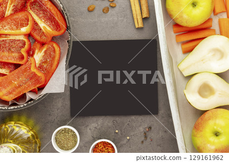 Empty black board with fresh vegetables and fruits on baking trays with spices and olive oil on marble kitchen table. Vegan and vegetarian diet. Cooking and eating at home. Veganuary. Flat lay 129161962