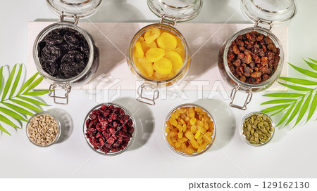 Dry fruits, nuts and seeds assortment on a blue background with palm leaves. Healthy snack - mix of organic nuts and dry fruits in a glass bowls. Vegan and vegetarian products. Flat lay Dry fruits, nuts and seeds assortment on a blue background with palm leaves. Healthy snack - mix of organic nuts and dry fruits in a glass bowls. Vegan and vegetarian products. Flat lay 129162130