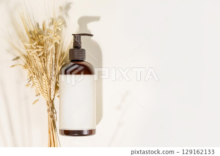 Natural beauty product. Mockup. Dispenser bottle with beauty product on a light background with rye and wheat bouquet and copy space. Mock up of natural washing gel. Flat lay 129162133