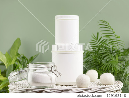Natural laundry detergent mockup. Washing detergent concept with bottles of washing gel or fabric softener on a white laundry basket on a green background with house plants. Laundry day 129162148