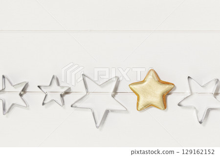 Cooking holiday cookies. Bakery flat lay. Ginger cookie in the form of stars, covered with gold glaze and cookie cutters on a white wooden background. Christmas and New Year Food 129162152