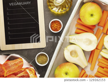 Black board with inscription Veganuary with fresh vegetables and fruits on baking trays with spices and olive oil on marble kitchen table. Vegan and vegetarian diet. Cooking and eating at home Black board with inscription Veganuary with fresh vegetables and fruits on baking trays with spices and olive oil on marble kitchen table. Vegan and vegetarian diet. Cooking and eating at home 129162153