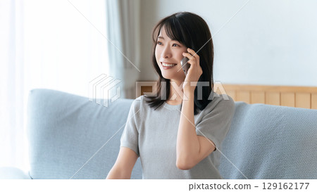 微笑的女人坐在沙發上用智慧型手機聊天 微笑的女人坐在沙發上用智慧型手機聊天 129162177