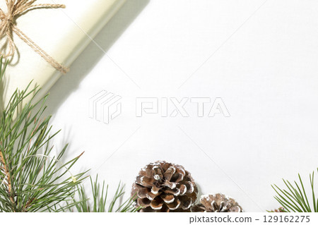 Winter holidays background. Fir branches with cones and a gift on a white textile background with copy space. Christmas and New Year flat lay 129162275