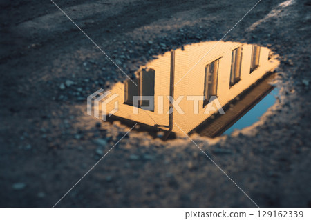 The reflection of a building in a puddle on a dirt road 129162339