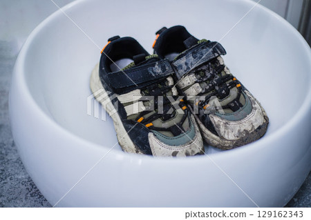 Children's dirty sneakers are lying in a white sink. Mud after a walk Children's dirty sneakers are lying in a white sink. Mud after a walk 129162343