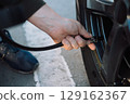 Person's hand inflating a car tire with an air compressor, checking pressure 129162367