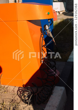 Vibrant orange air pump station for tire inflation with a pressure gauge and black hose 129162368