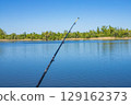 Fishing rod extends towards the water on a sunny day, capturing a beautiful outdoor scene 129162373