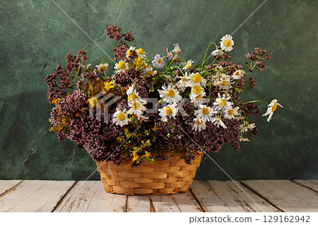 Flower arrangement of wild medicinal herbs on a wooden table in a basket, a bouquet of St. John's wort, oregano, mint, chamomile, a collection of useful herbs for treatment according to folk recipes Flower arrangement of wild medicinal herbs on a wooden table in a basket, a bouquet of St. John's wort, oregano, mint, chamomile, a collection of useful herbs for treatment according to folk recipes 129162942