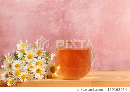 Chamomile tea or infusion in transparent glasses with natural small chamomile flowers on wooden table, concept of medicinal herbal tea and proper natural nutrition, summer postcard Chamomile tea or infusion in transparent glasses with natural small chamomile flowers on wooden table, concept of medicinal herbal tea and proper natural nutrition, summer postcard 129162954