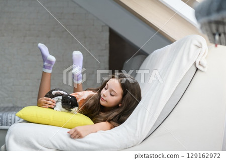 Girl lying on sofa and hugging rabbit on pillow. 129162972