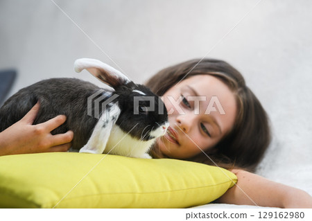 Girl lying on sofa and hugging rabbit on pillow. 129162980