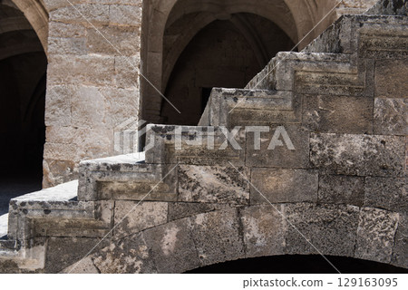 Historic stone courtyard with arched staircases, ancient sculptures in a Mediterranean old town 129163095