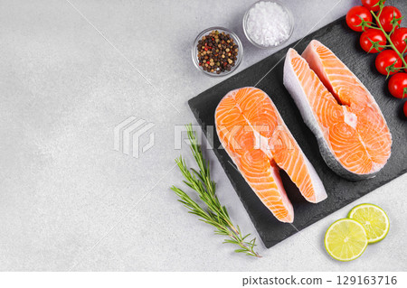 Two fresh raw salmon, trout steak with tomatoes, spices, rosemary and lime on white stone background Two fresh raw salmon, trout steak with tomatoes, spices, rosemary and lime on white stone background 129163716