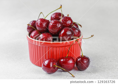 Red bowl full of fresh organic sweet cherries on white stone background, healthy summer snack Red bowl full of fresh organic sweet cherries on white stone background, healthy summer snack 129163726