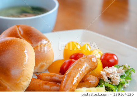 A Western-style breakfast set featuring bread rolls, sausages, salad, and fruit A Western-style breakfast set featuring bread rolls, sausages, salad, and fruit 129164120
