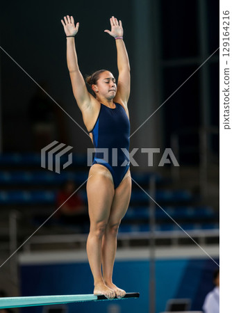 Diver poised on springboard, preparing for a graceful dive into the water below 129164216