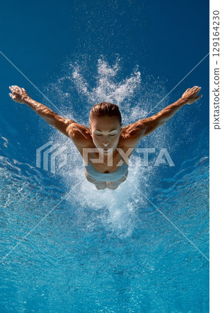 Diver gracefully plunges into clear blue water, showcasing athleticism and precision in motion 129164230