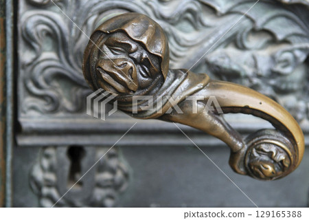 Doorhandle with grimace face and lock at a side portal of the cathedral of Cologne, NRW, Germany Doorhandle with grimace face and lock at a side portal of the cathedral of Cologne, NRW, Germany 129165388