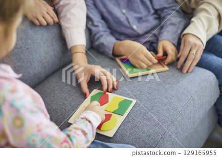 Children playing with colorful jigsaw puzzle on sofa while adults helping during family leisure. 129165955
