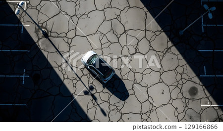 Aerial View Of White Vehicle Parked On Cracked Asphalt Surface With Shadows And Directional Markings 129166866