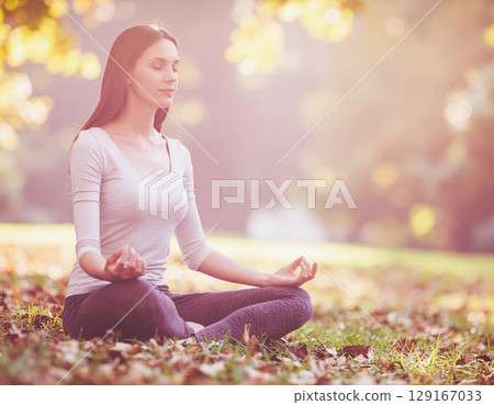 A woman meditating in a park with nature 129167033