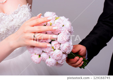 Hands of bride and groom with rings on wedding bouquet. Marriage concept. 129168745