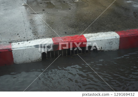 red and white curb road with drain hole in the rainy day 129169432