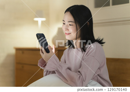 一位年輕女子在床上操作智慧型手機生活風格影像 129170140