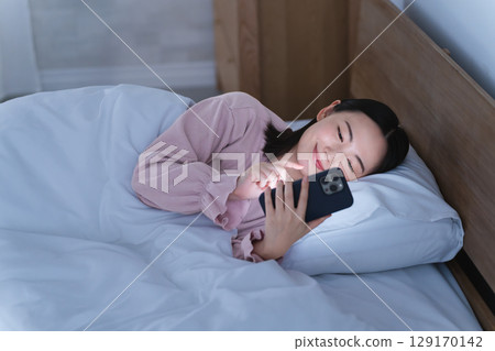 一位年輕女子在床上操作智慧型手機生活風格影像 一位年輕女子在床上操作智慧型手機生活風格影像 129170142