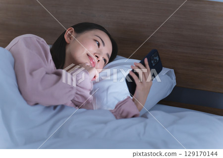 一位年輕女子在床上操作智慧型手機生活風格影像 129170144