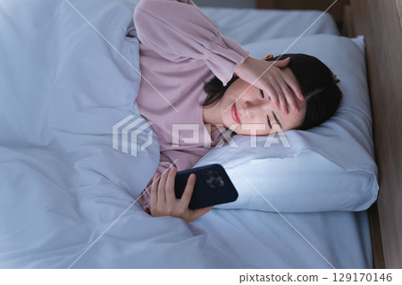 A young woman operating a smartphone in bed Lifestyle image 129170146