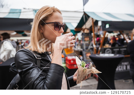 Beautiful young woman holding delicious organic salmon vegetarian burger and drinking homebrewed IPA beer on open air beer an burger urban street food festival in Ljubljana, Slovenia Beautiful young woman holding delicious organic salmon vegetarian burger and drinking homebrewed IPA beer on open air beer an burger urban street food festival in Ljubljana, Slovenia 129170725