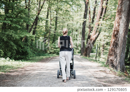 Rear view of casually dressed mother walking with baby stroller in Koseski bajer city park in Ljubljana, Slovenia. Family, child and parenthood concept. 129170805