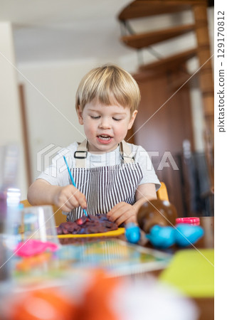 Blond boy sculpts from plasticine at home at the table. The idea and concept of the school, home education and developmental activities. 129170812