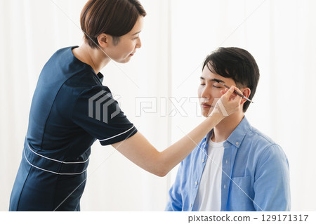 一位年輕男士正在接受化妝師的修眉美容形象 一位年輕男士正在接受化妝師的修眉美容形象 129171317