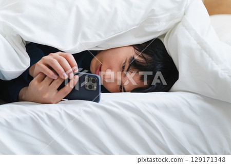 A young man wrapped in a futon and operating a smartphone Lifestyle image A young man wrapped in a futon and operating a smartphone Lifestyle image 129171348