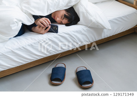 A young man wrapped in a futon and operating a smartphone Lifestyle image 129171349