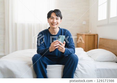 A young man operating a smartphone on his bed Lifestyle image A young man operating a smartphone on his bed Lifestyle image 129171566