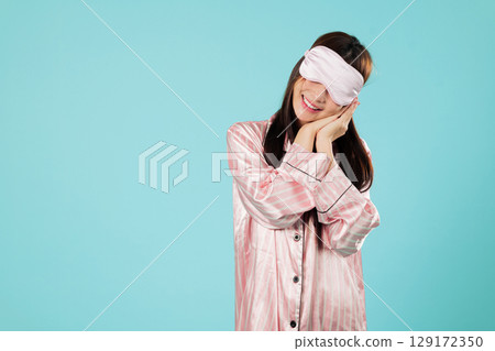 Dreamy asian woman in sleepwear, cover eye with a sleep mask, hands folded, smile, and she rests at home ready for a good night sleep and relaxation, headshots isolated studio blue background Dreamy asian woman in sleepwear, cover eye with a sleep mask, hands folded, smile, and she rests at home ready for a good night sleep and relaxation, headshots isolated studio blue background 129172350