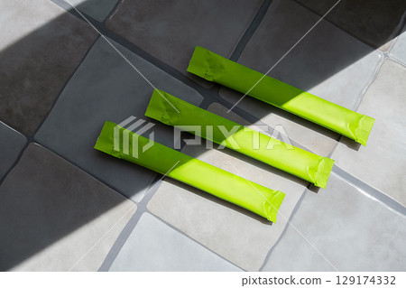 Three green plastic packaging sticks on tile floor with sunlight and shadow. 129174332