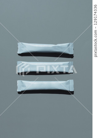 Three grey sachets with shadow on monochrome background. 129174336